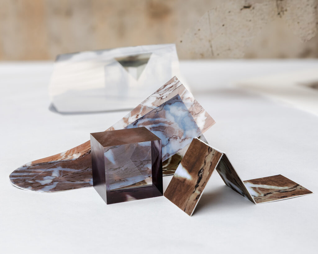 Close-up of two folded photos of stone-like textures, under a translucent brown cube