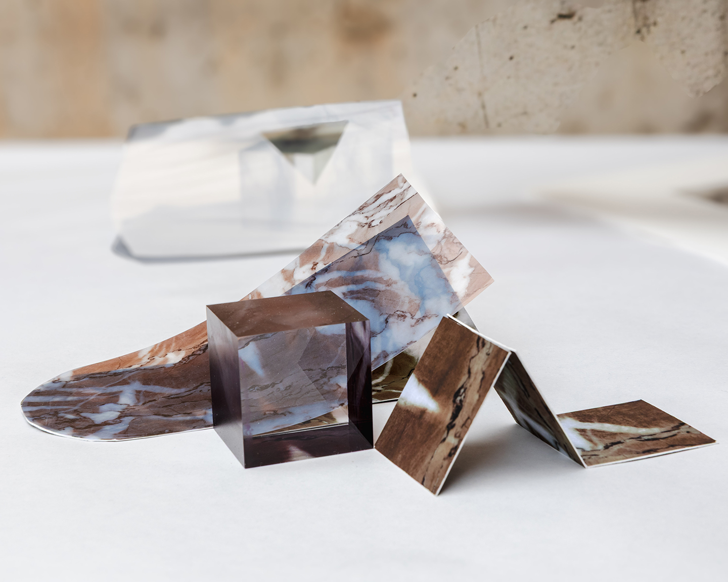 Close-up of two folded photos of stone-like textures, under a translucent brown cube